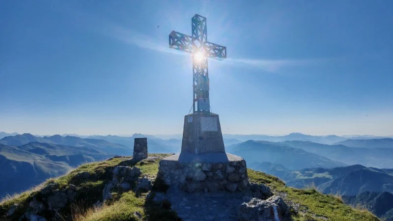 Croce di vetta del Monte Alben con il sole alle spalle e panorama