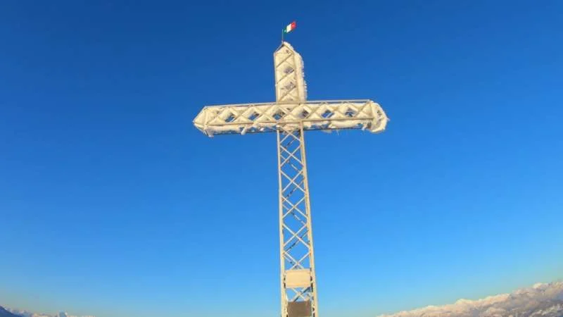 Croce di vetta del Monte Linzone con bandiera sotto il cielo blu